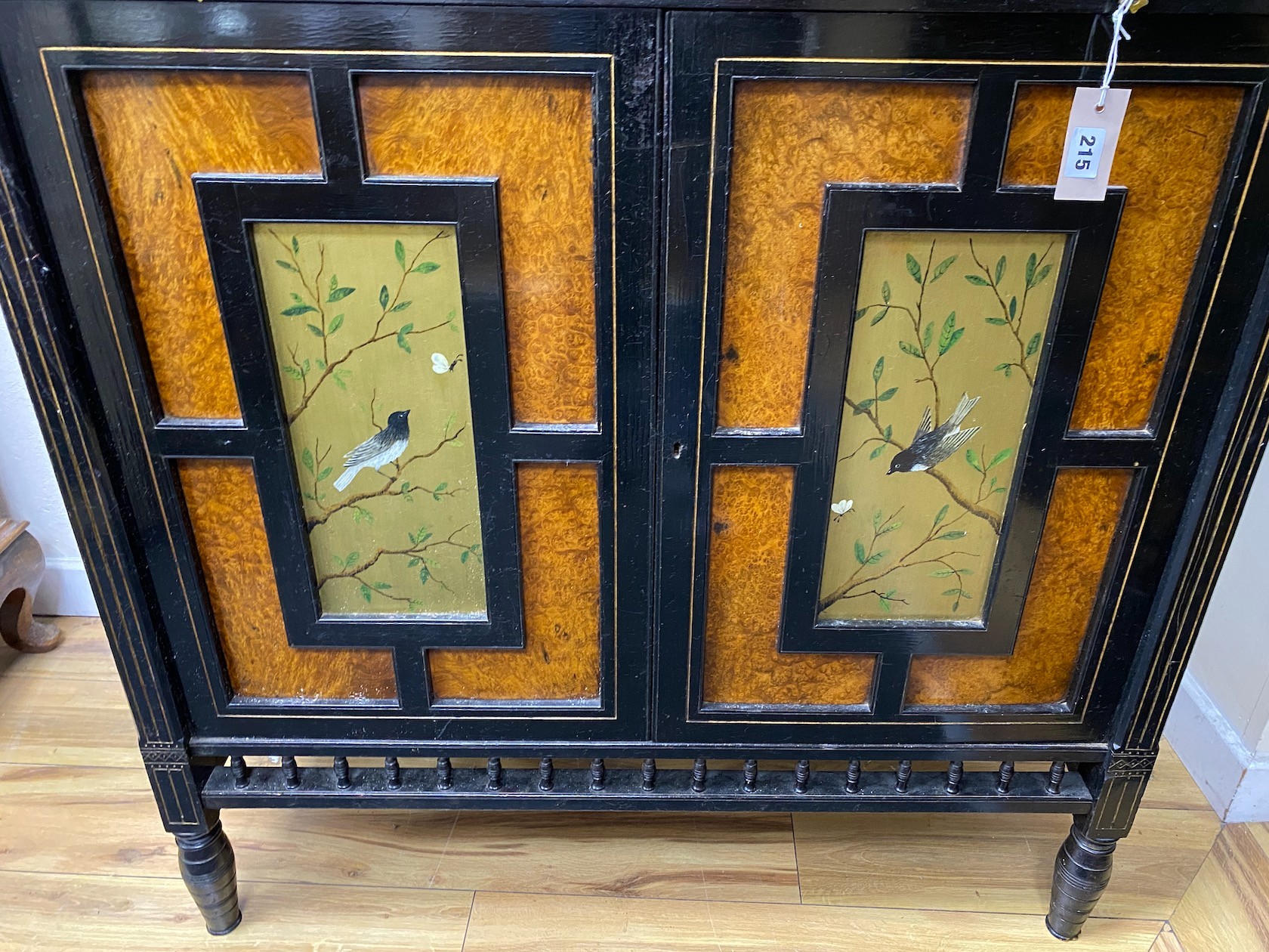 A Victorian aesthetic movement ebonised and bird's eye maple two door side cabinet, inset painted panels of birds, width 99cm, depth 44cm, height 141cm